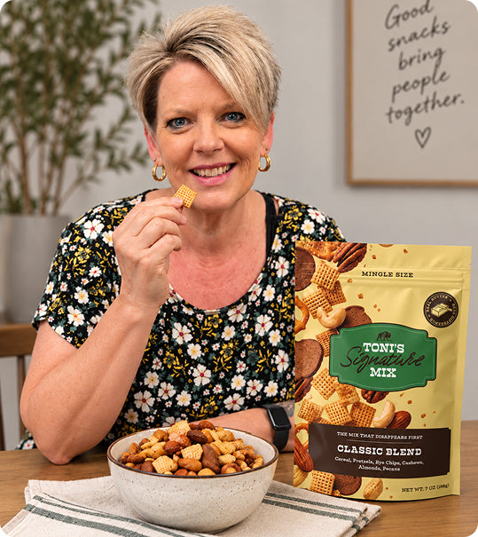 Toni holding a piece of the mix at a table, with a bowl of it and a Classic Blend bag in front of her.